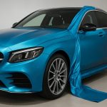 A blue luxury car with a flowing fabric draped over it, highlighting its glossy finish.
